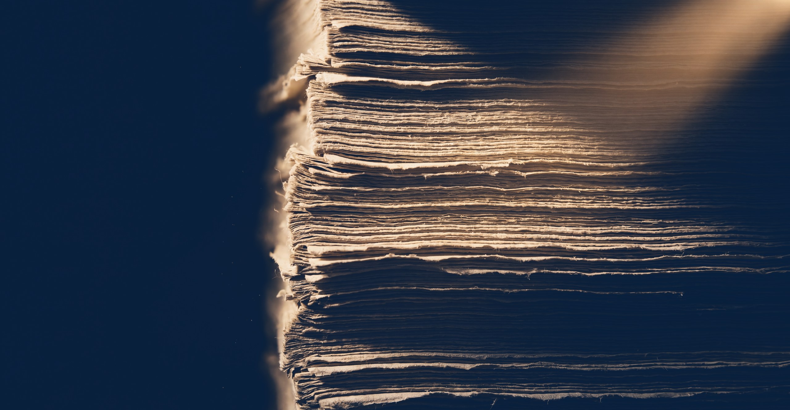 Raking light across the layered edges of archival paper