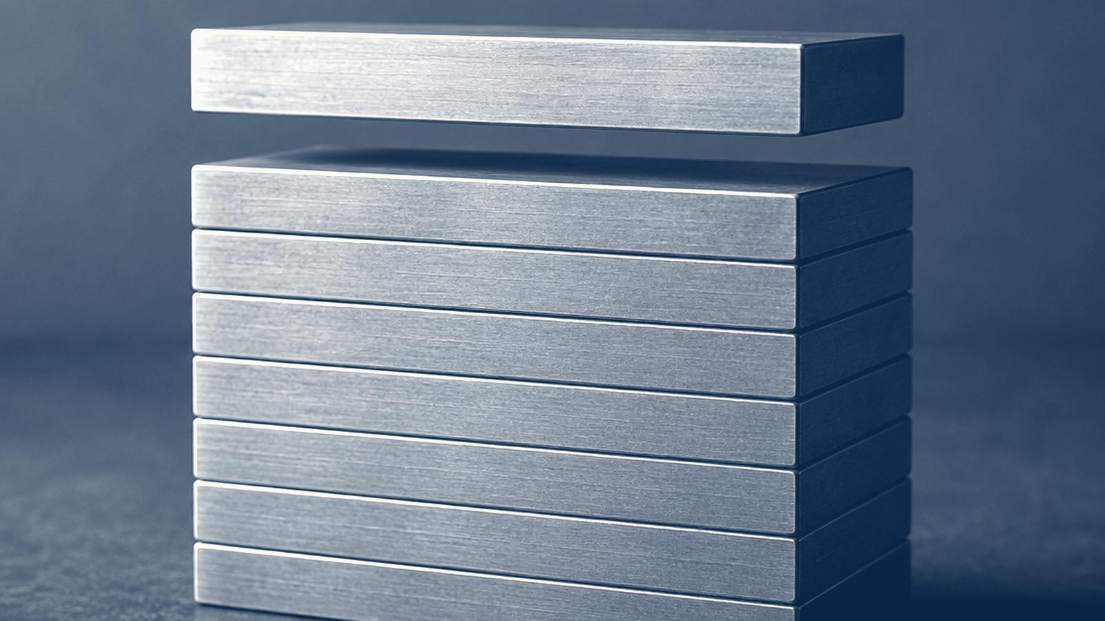 A stack of brushed-metal bars with the top bar suspended above the rest, on a dark ground