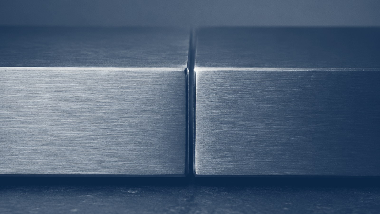 Two brushed-metal blocks meeting at a single lit seam, on a dark ground